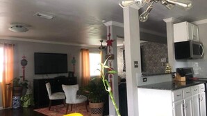Un salon moderne comprenant un coin repas, une cuisine et un téléviseur fixé au mur.