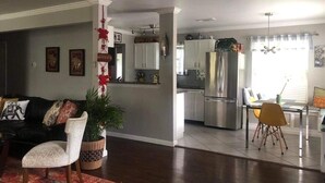 Un salon avec un canapé, un coin repas avec une table et des chaises, une cuisine équipée de meubles et d’appareils électroménagers, et un escalier menant à l’étage supérieur.