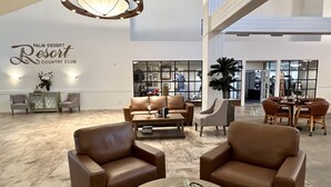 A spacious lobby with leather sofas, a coffee table, and a large chandelier. A sign reads "Palm Desert Resort Country Club." - Relaxing desert retreat with amazing mountain and lake view on the 7th fairway! (Palm Desert)