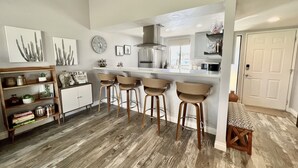 A modern kitchen with a bar area, wooden flooring, and a dining area with a table and chairs. - Relaxing desert retreat with amazing mountain and lake view on the 7th fairway! (Palm Desert)