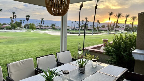 A patio with a table and chairs, a hanging light fixture, and a view of a golf course and palm trees. - Relaxing desert retreat with amazing mountain and lake view on the 7th fairway! (Palm Desert)