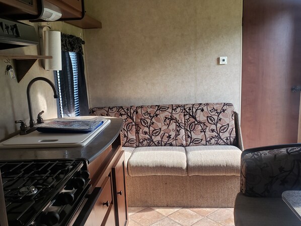 A compact kitchen with a gas stove, a sink, and a patterned sofa. - Camping with goats (Columbia Falls)