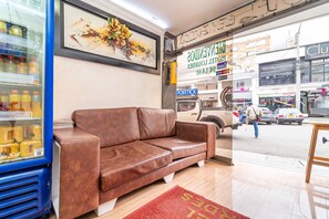 A brown leather sofa in a lobby with a blue refrigerator stocked with beverages, a red rug, and a large abstract painting on the wall. - Hotel Lourdes La 62 (Bogotá)