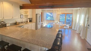 A spacious kitchen with a large island, bar stools, and a view of the outdoors through large windows.