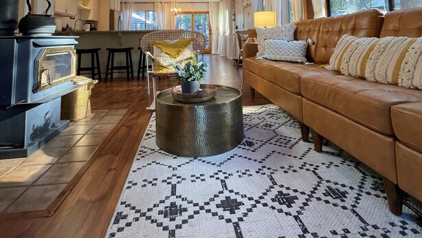 A spacious living area with a high ceiling, wooden beams, a central round coffee table, a leather sofa, and large windows providing natural light.