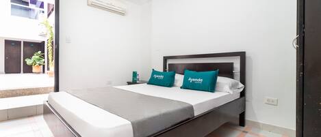 Una habitación de hotel con cama, mesita de noche, ventana y puerta.