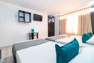 Habitación de hotel con dos camas individuales, un televisor montado en la pared, una mesita con una botella y una puerta con un cartel.