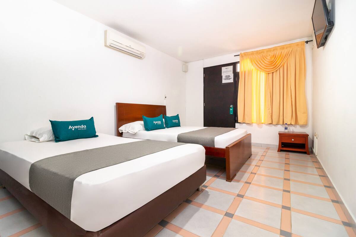 A hotel room with two beds, a wooden headboard, a small wooden nightstand, and a TV mounted on the wall.