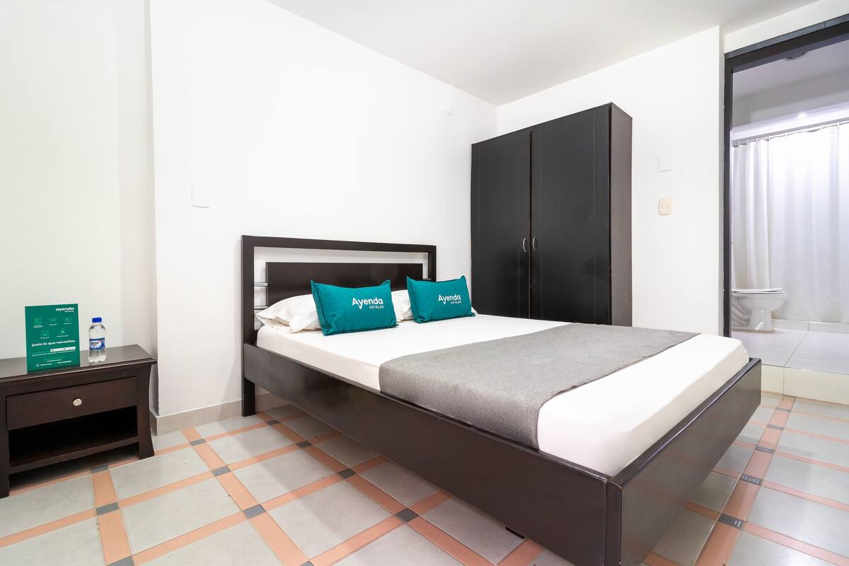 A hotel room with a bed, a wardrobe, a nightstand, and a bathroom visible through an open door.
