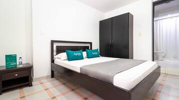 Habitación de hotel con cama, armario, mesita de noche y baño visible a través de una puerta abierta.