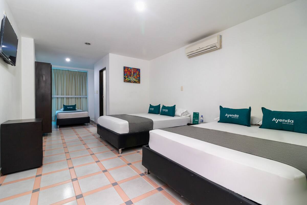 A hotel room with two beds, a TV, an air conditioner, and a colorful painting on the wall.