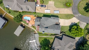 Ovenfra ses et boligområde med swimmingpool, en mole og en indkørsel, der fører til et hus med garage.