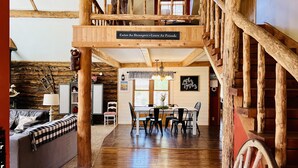 Un interior rústico con una escalera de madera, un comedor y un letrero que dice 'Enter As Strangers Leave As Friends'.