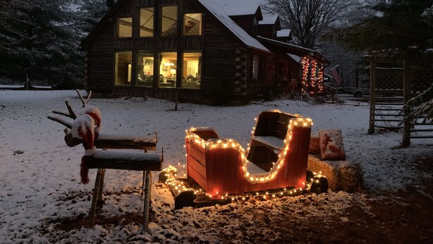Una cabaña de troncos con ventanas amplias y un patio cubierto de nieve.