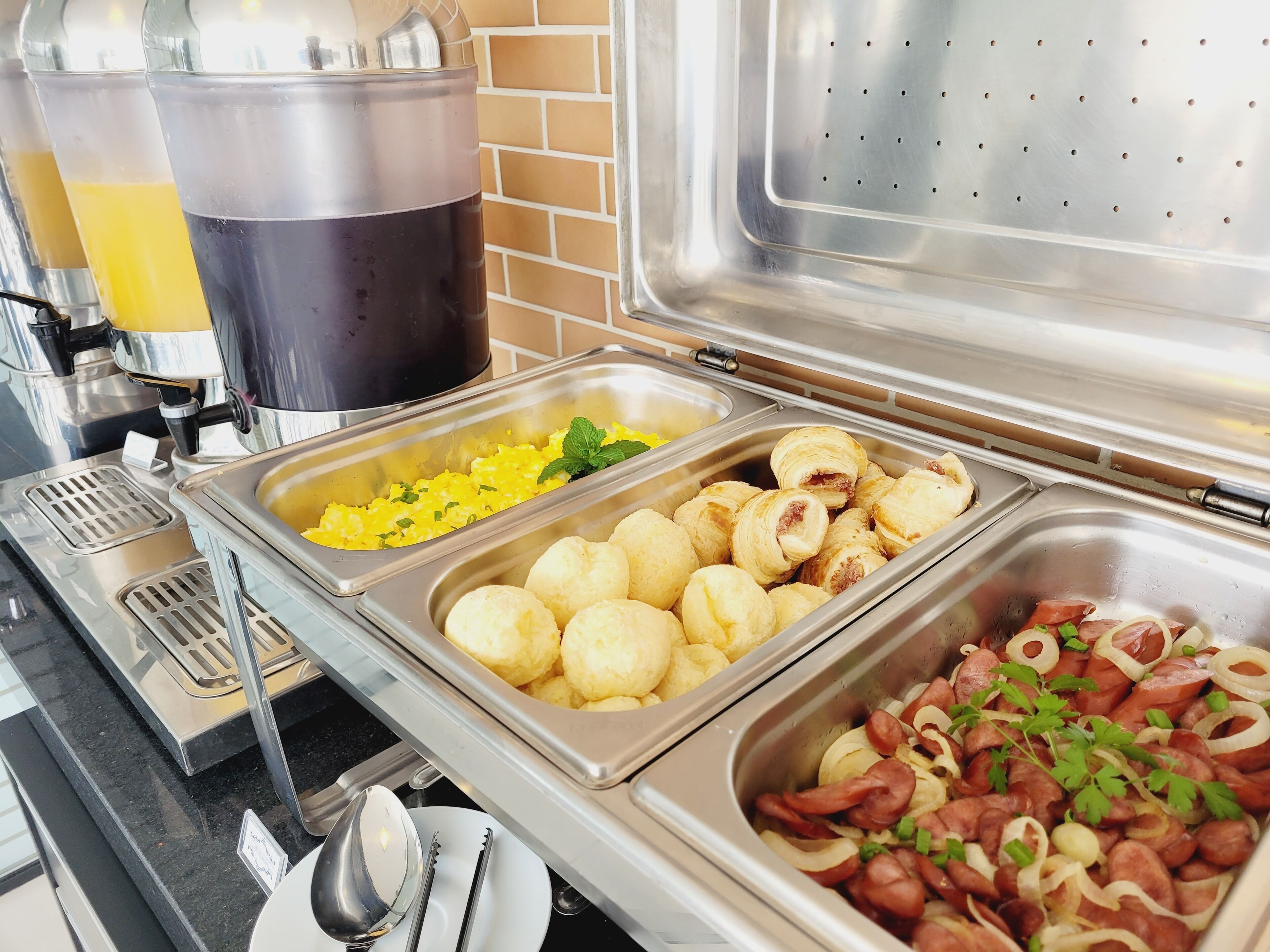 Un bufé con diversas opciones de comida, como huevos revueltos, bolitas de queso y salchichas.