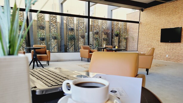 Un espacio exterior moderno con asientos, una laptop, una taza de café y un menú.