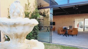 Un espacio exterior moderno con una fuente de piedra, asientos y una pared de vidrio que refleja el interior.