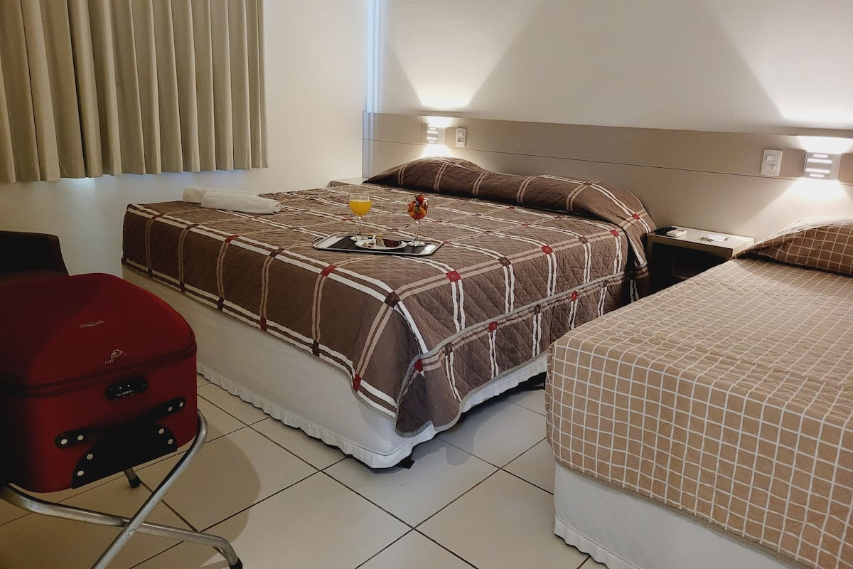Una habitación de hotel con una cama, una maleta roja y una mesita de noche con una lámpara.