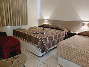 Una habitación de hotel con una cama, una maleta roja y una mesita de noche con una lámpara.