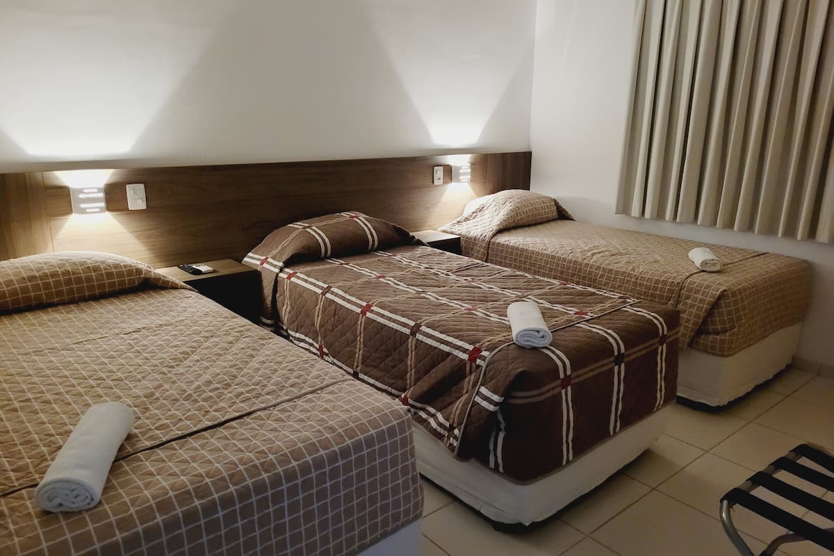 Habitación de hotel con dos camas, cada una con cubrecama acolchado y almohadas, una mesita de noche con lámpara y una silla.