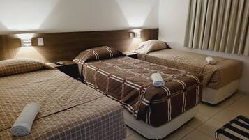 A hotel room with two beds, each with a quilted bedspread and pillows, a nightstand with a lamp, and a chair.