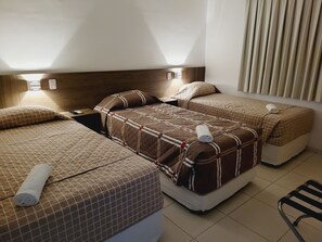 Habitación de hotel con dos camas, cada una con cubrecama acolchado y almohadas, una mesita de noche con lámpara y una silla.