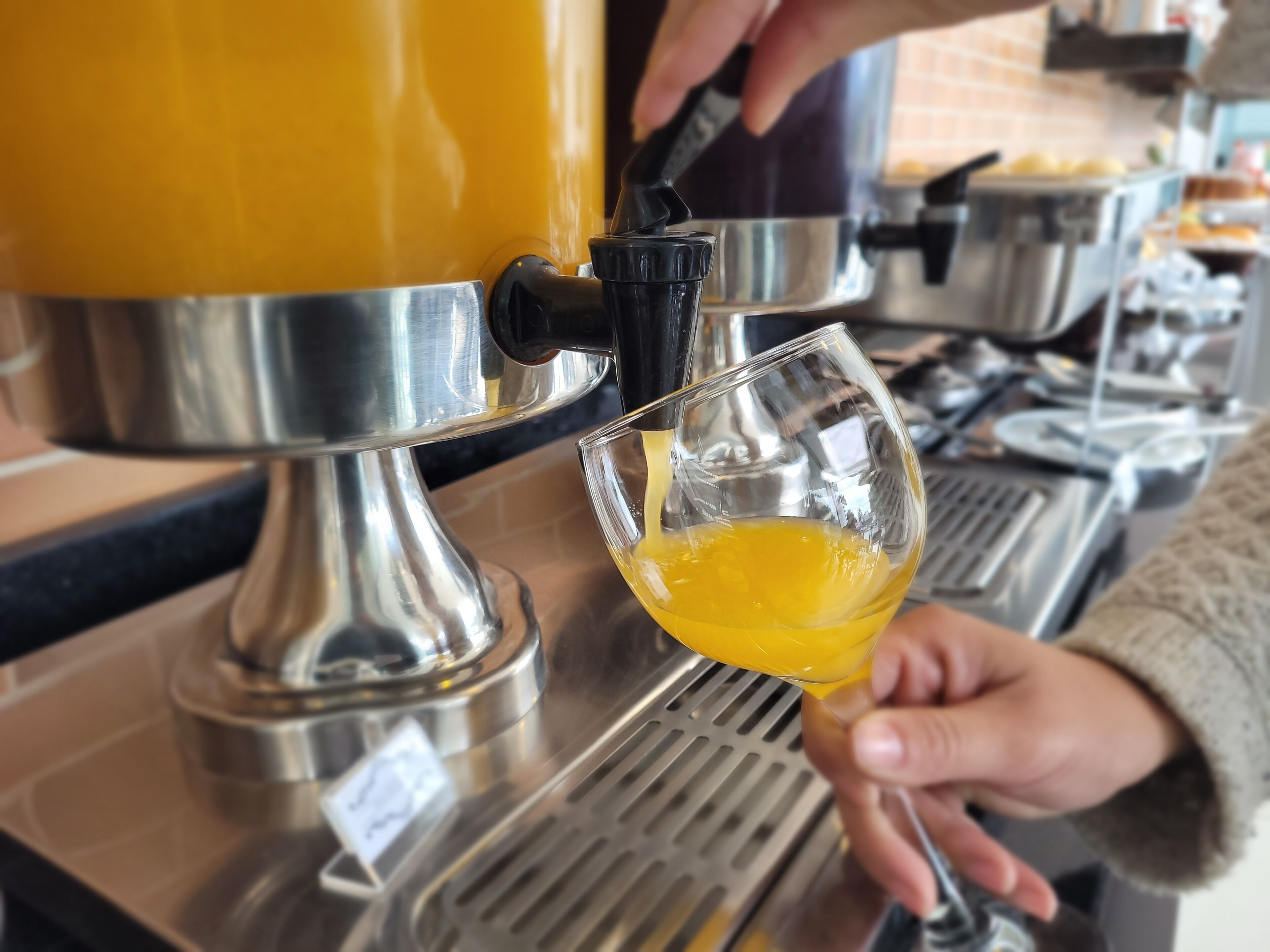 A person pouring a yellow liquid from a machine into a glass.