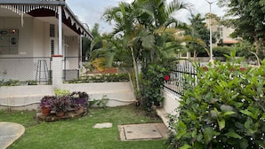 A residential building with a covered porch, a fenced garden, and various plants.