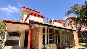 A two-story house with a tiled roof, a balcony with a railing, and a small garden area with potted plants.