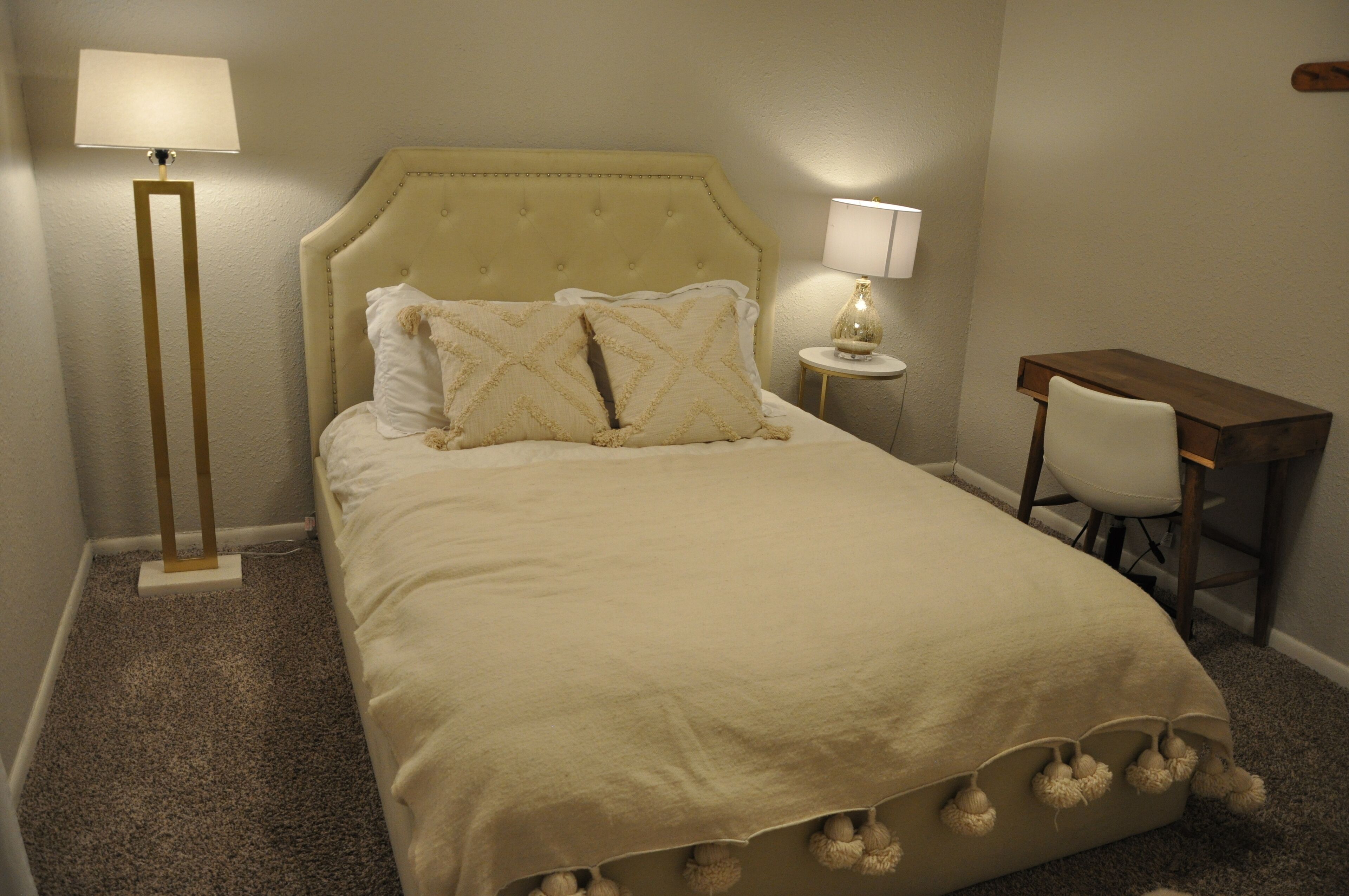 Un lit bien fait, avec une tête de lit, une lampe de chevet, une petite table avec une lampe et une chaise.