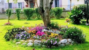 Un jardin bien entretenu, agrémenté de nombreuses fleurs aux couleurs vives et d’un arbre au centre.