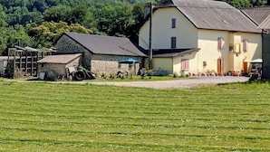 Un cadre rural avec une grande maison, un petit bâtiment en pierre et un champ.