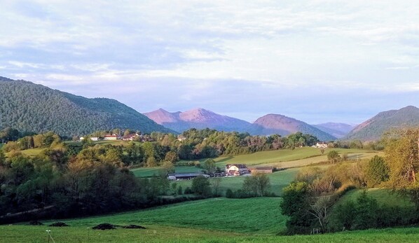 Un paysage rural caractérisé par des collines douces, des maisons éparpillées et une chaîne de montagnes en arrière-plan.