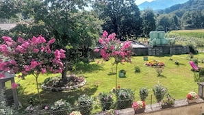 Un jardin bien entretenu, agrémenté de diverses plantes à fleurs, d’une pelouse et d’un espace détente avec des chaises et un parasol.