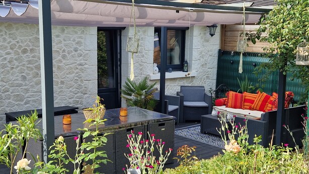 A patio with outdoor furniture, a stone wall, and a green fence. - Charm restored (SEUR)