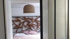 A bedroom with a bed, a woven headboard, a woven hanging light fixture, and a textured rug. - Charm restored (SEUR)