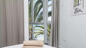 A hotel room with a bed, a window with curtains, and a wall with a framed artwork. - Apartment on the Beach with Sea Views, Balcony, Shared Pool & WiFi (Nerja)