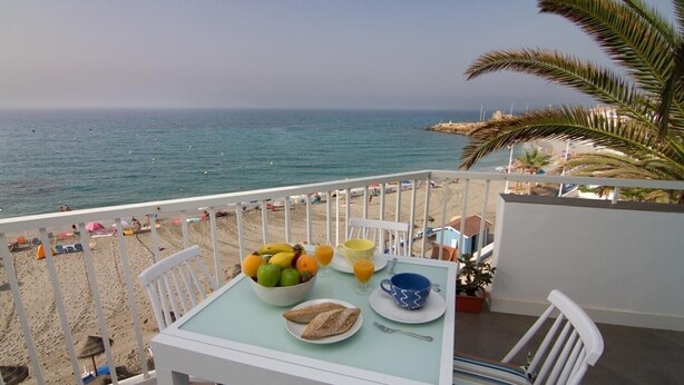 A balcony with a table set for breakfast, overlooking a beach. - Apartment on the Beach with Sea Views, Balcony, Shared Pool & WiFi (Nerja)