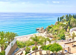 Paesaggio costiero con spiaggia, affioramenti rocciosi e vegetazione lussureggiante.