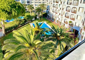 A hotel courtyard with a swimming pool, palm trees, and a multi-story building with balconies. - Apartment with Sea Views, Beachfront, Shared Pool, A/C and WiFi (Nerja)