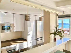 Et moderne køkken med stålemmer, et glasbryggerspanel og havudsigt.