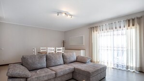 A modern living room with a grey sectional sofa, a wooden coffee table, and a dining area with a white table and chairs.