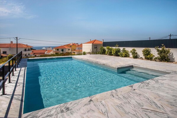 A rectangular swimming pool with clear blue water, surrounded by a marble deck.