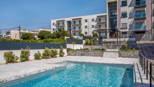 A swimming pool with a modern design, surrounded by a landscaped area with steps leading to a building with balconies.
