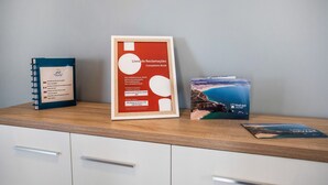 A desk with a framed complaints book, a spiral notebook, and a travel brochure.