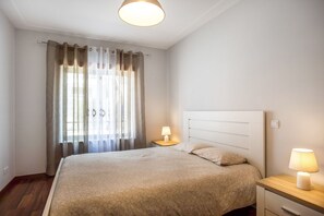 A bedroom with a bed, two bedside lamps, a nightstand, and a window with curtains.