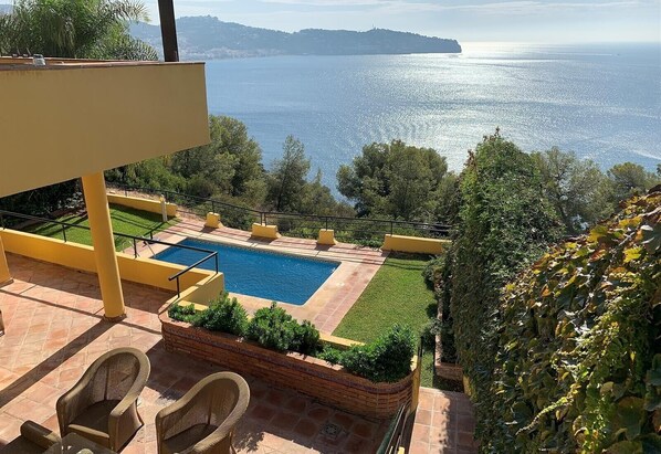 Area piscina con vista sul mare, arredi da esterno e giardino curato.