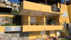 A two-story building with a yellow facade, a balcony with a metal railing, and a stone wall with plants. - Villa "Casa Heidi" with Sea View, Pool, Balcony, Air Conditioning & Wi-Fi (Almunecar)
