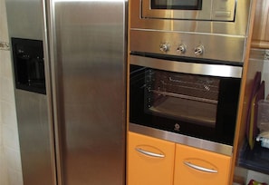 Un refrigerador y horno de acero inoxidable, con un microondas encima, integrados en un mueble de cocina.