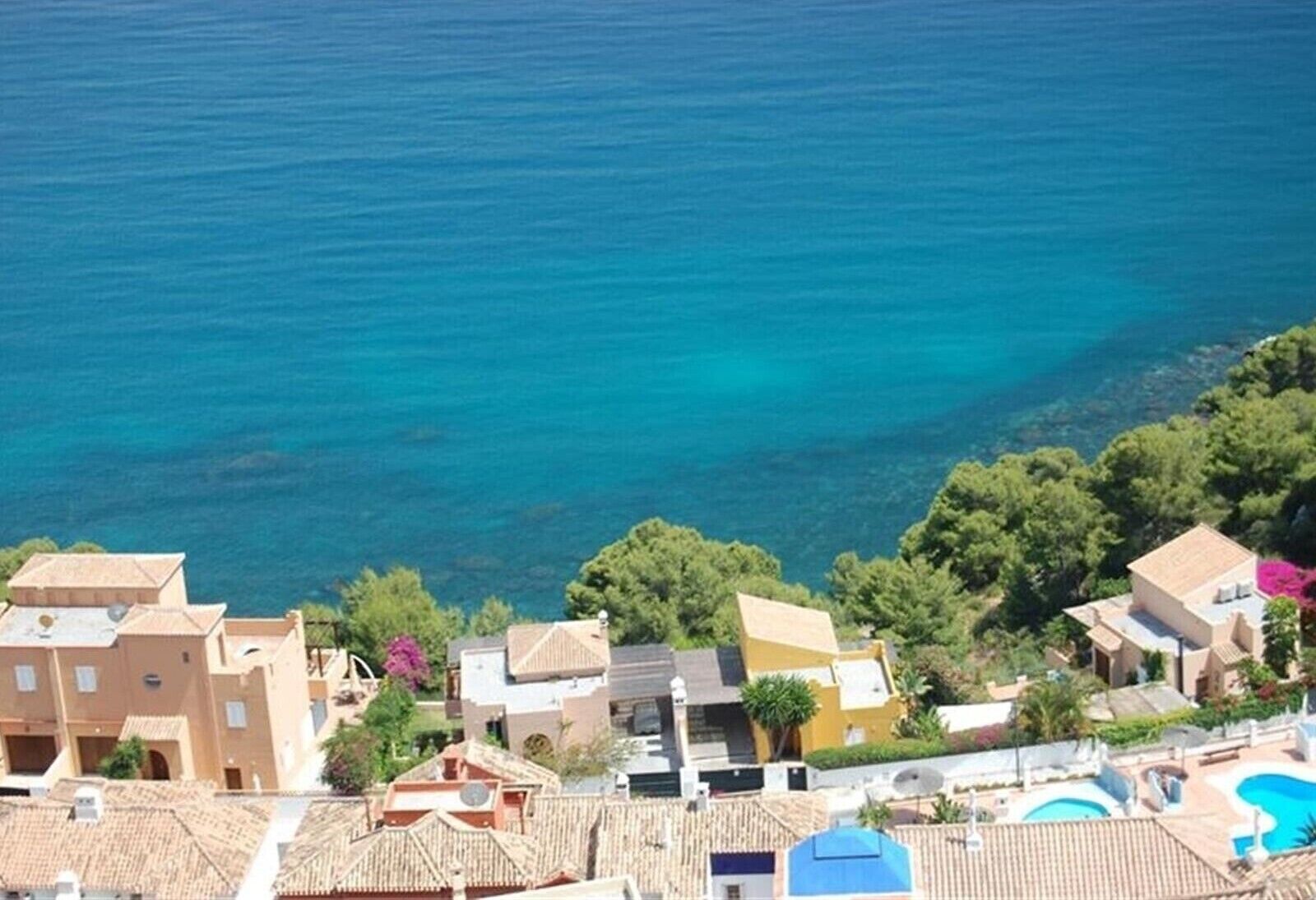 Zona residencial a la costa amb cases, una piscina i vistes al mar.